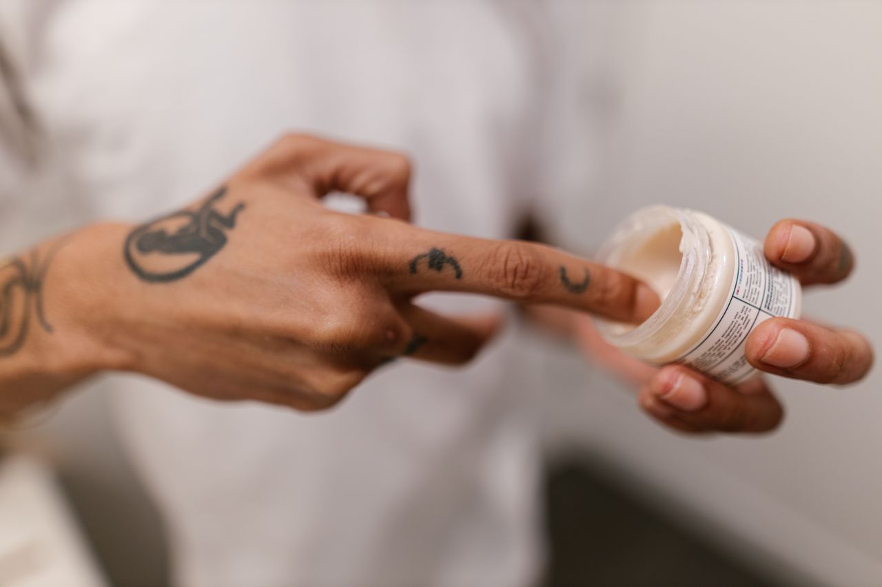 Close-up of a tattooed hand applying cream, emphasizing skincare and personal grooming.
