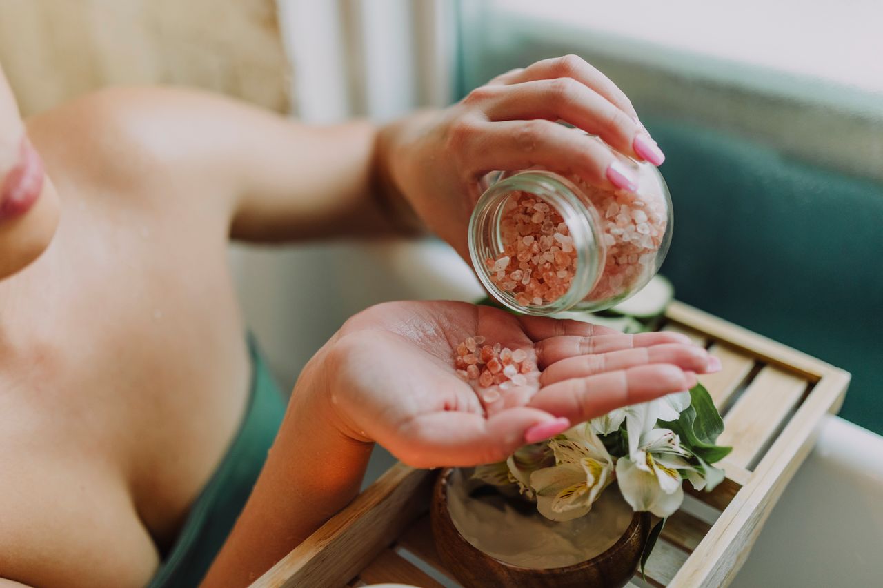 Close-up of hands pouring pink bath salt with flowers in a relaxing spa setting.